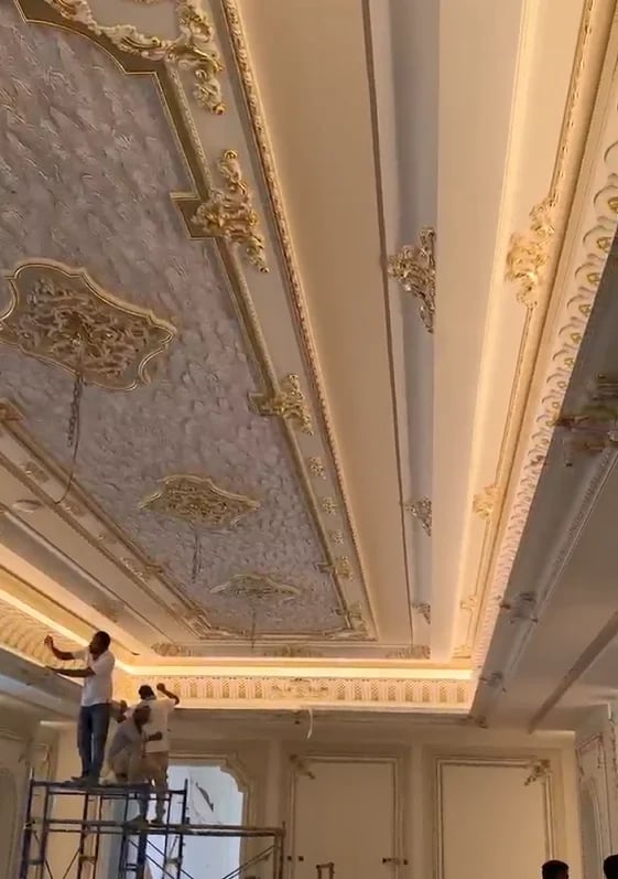 Workers on scaffolding restoring ornate gold and cream decorated ceiling with classical architectural details and recessed panels