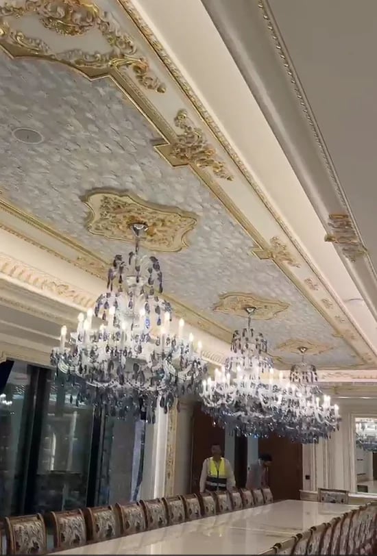 Ornate dining room with gold-trimmed ceiling, crystal chandeliers, and formal table seating with patterned chairs